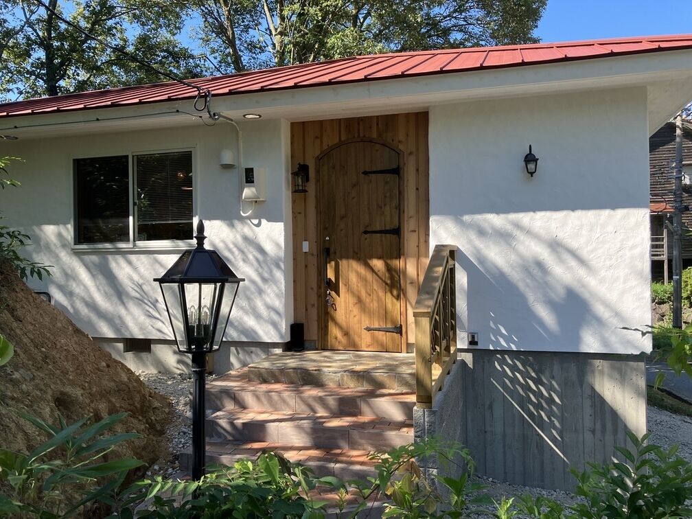 Une maison avec un toit rouge, une porte d’entrée en bois, une lanterne noire et une fenêtre.