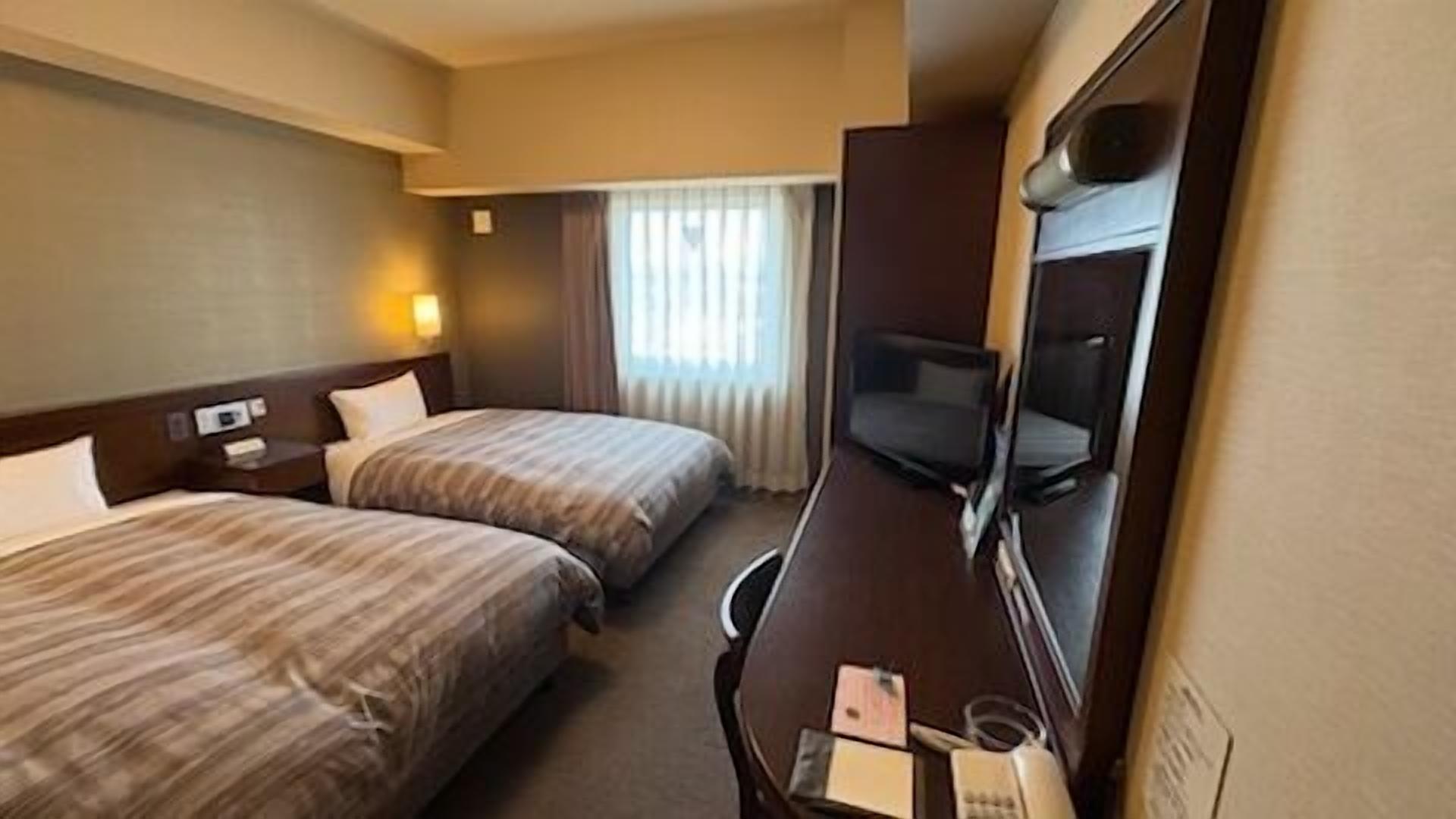 Habitación de hotel con dos camas, un escritorio, un televisor y una ventana con cortinas.