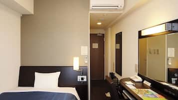 A hotel room with a bed, a desk, a mirror, an air conditioning unit, and a door leading to another room.