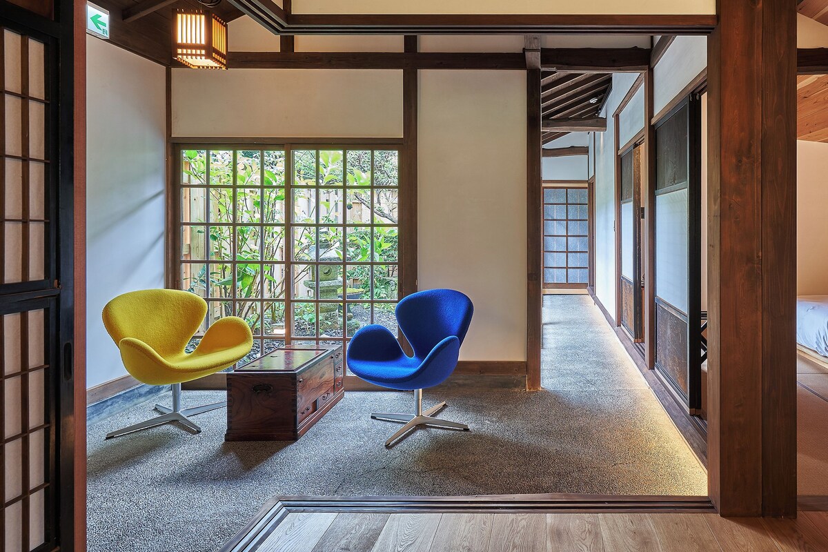 Una habitación japonesa tradicional con suelo de tatami, una cama de madera baja y dos sillas modernas.
