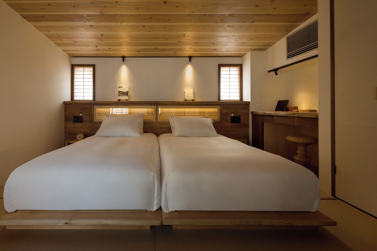 Una cama doble con cabecera de madera, dos mesitas de noche y un ventanal con vistas.