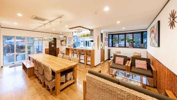 A spacious room with a wooden dining table, a sofa with cushions, and a large window offering a view.