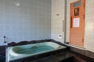 Een spa ruimte met een rechthoekig bad, betegelde wanden en een houten deur met een bordje.