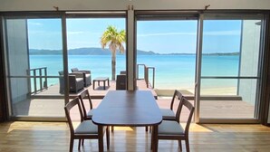 Um quarto espaçoso com uma grande porta de vidro deslizante que dá para uma varanda com vista para o mar e palmeiras.