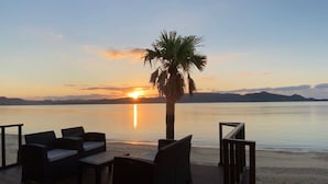 Terraço com área de estar ao ar livre e vista para um corpo d'água tranquilo ao pôr do sol.