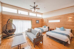 Una habitación tipo cabaña de madera con dos camas, un sillón colgante, un sofá y una mesa de madera.