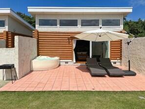Una casa moderna con un patio que incluye un jacuzzi, dos sillones de descanso y una sombrilla grande.