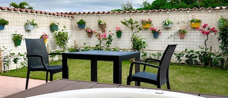 Un jacuzzi con dos sillas, una mesa y una pared con azulejos y plantas en macetas.