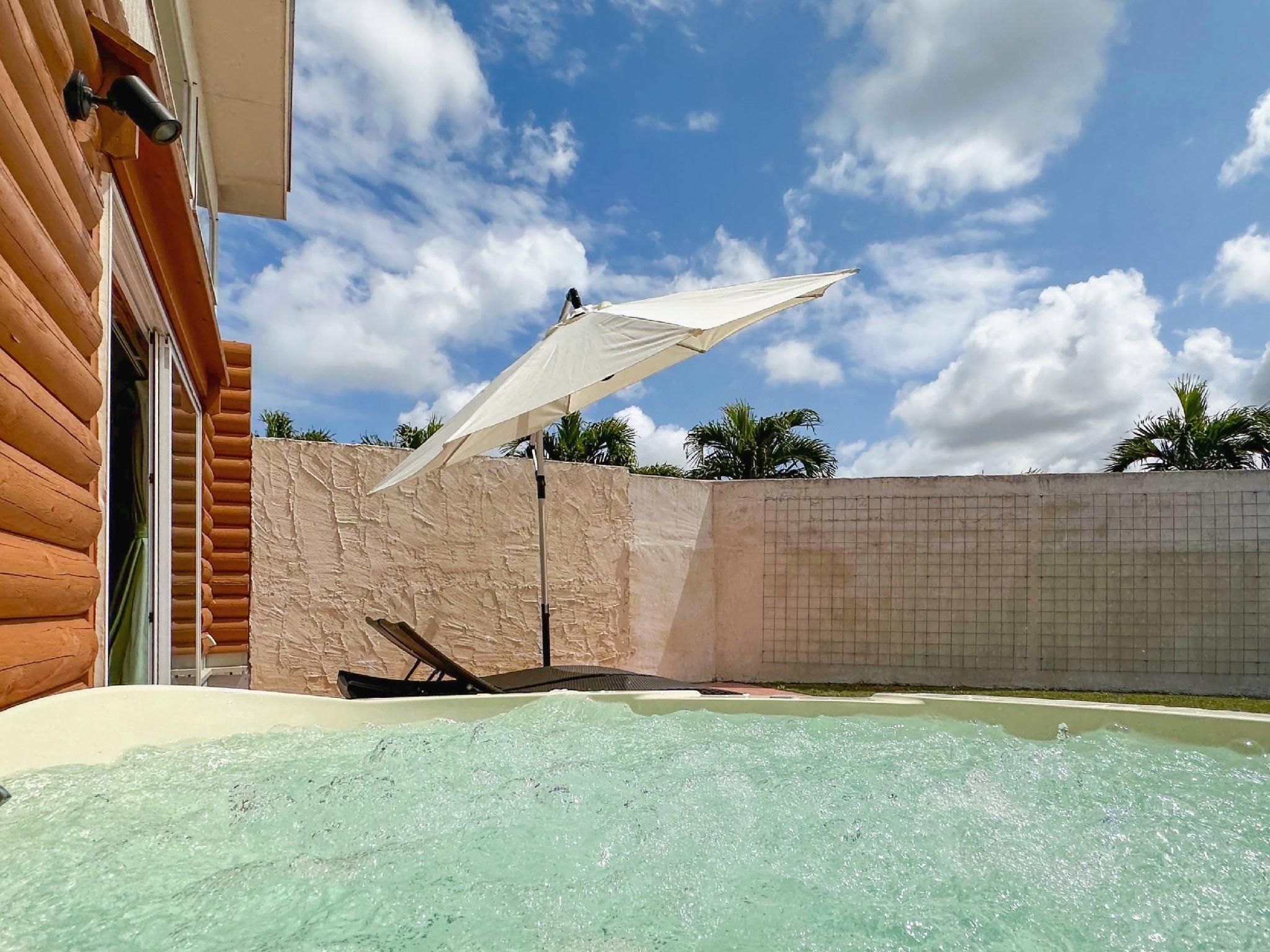 Un espace avec un jacuzzi, agrémenté d’un parasol blanc, de murs en bois et d’un ciel dégagé.