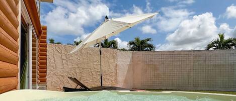 A hot tub area with a white umbrella, wooden walls, and a clear sky.