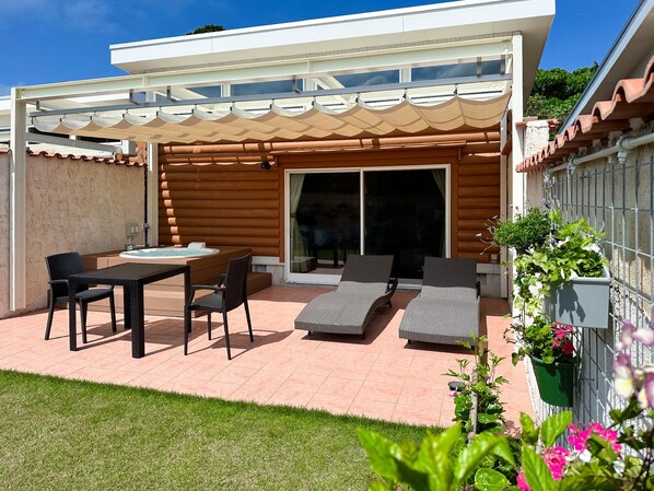 A covered patio with a table and chairs, a hot tub, and lounge chairs. - Tabino Hotel Villa Miyakojima (Miyakojima)