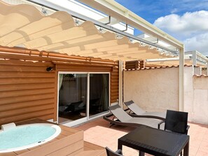 Un área de patio techada con un jacuzzi, sillones de descanso y una mesa.