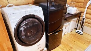 A compact, modern laundry room with a front-loading washing machine, a stacked dryer, and a vacuum cleaner. - Tabino Hotel Villa Miyakojima (Miyakojima)