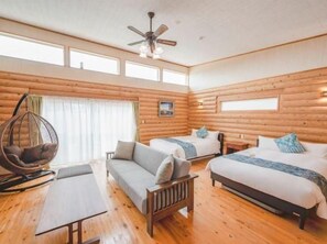 Habitación de cabaña de troncos con una cama, dos sofás, una silla colgante y un ventilador de techo.