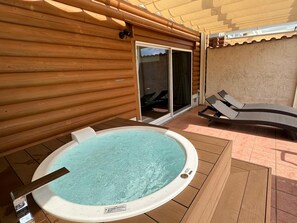 Un jacuzzi en una terraza de madera con un ventanal corredizo que da a un porche cubierto.
