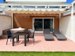 Un patio al aire libre con un jacuzzi, una mesa y sillas de descanso.