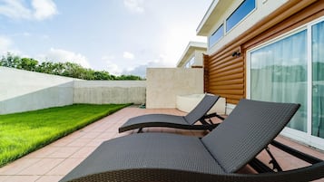 A patio area with two lounge chairs and a small table, a concrete wall, and a grassy lawn.