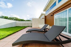 A patio area with two lounge chairs and a small table, a concrete wall, and a grassy lawn. - Tabino Hotel Villa Miyakojima (Miyakojima)
