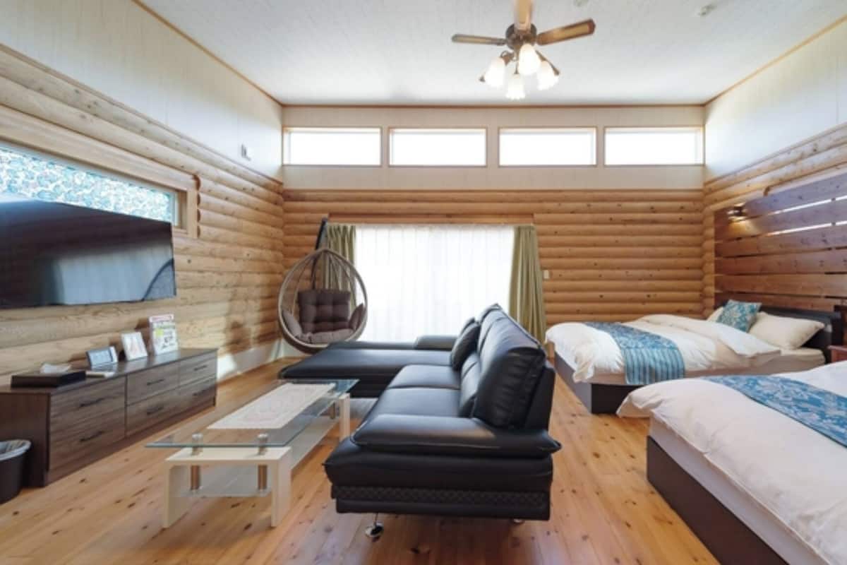 Un dormitorio de cabaña de madera con sofá, cama, sillón colgante y televisor.