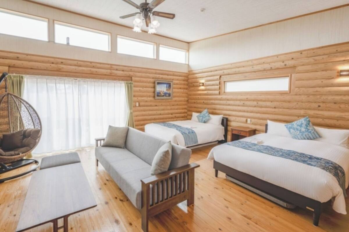 Una habitación tipo cabaña de madera con dos camas, un sillón colgante, un sofá y una mesa de madera.