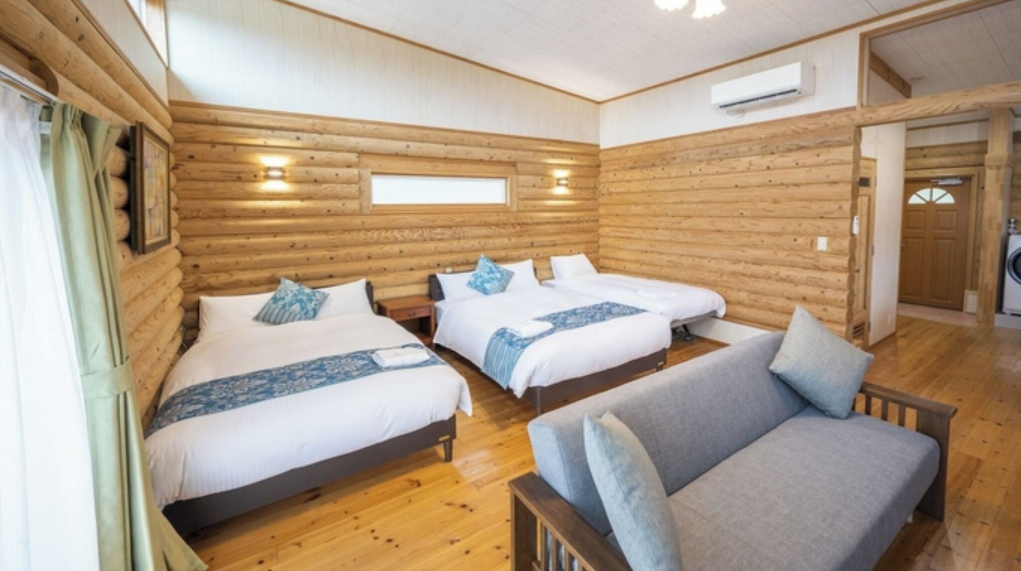 A wooden cabin room with three beds, a sofa, and a washing machine.