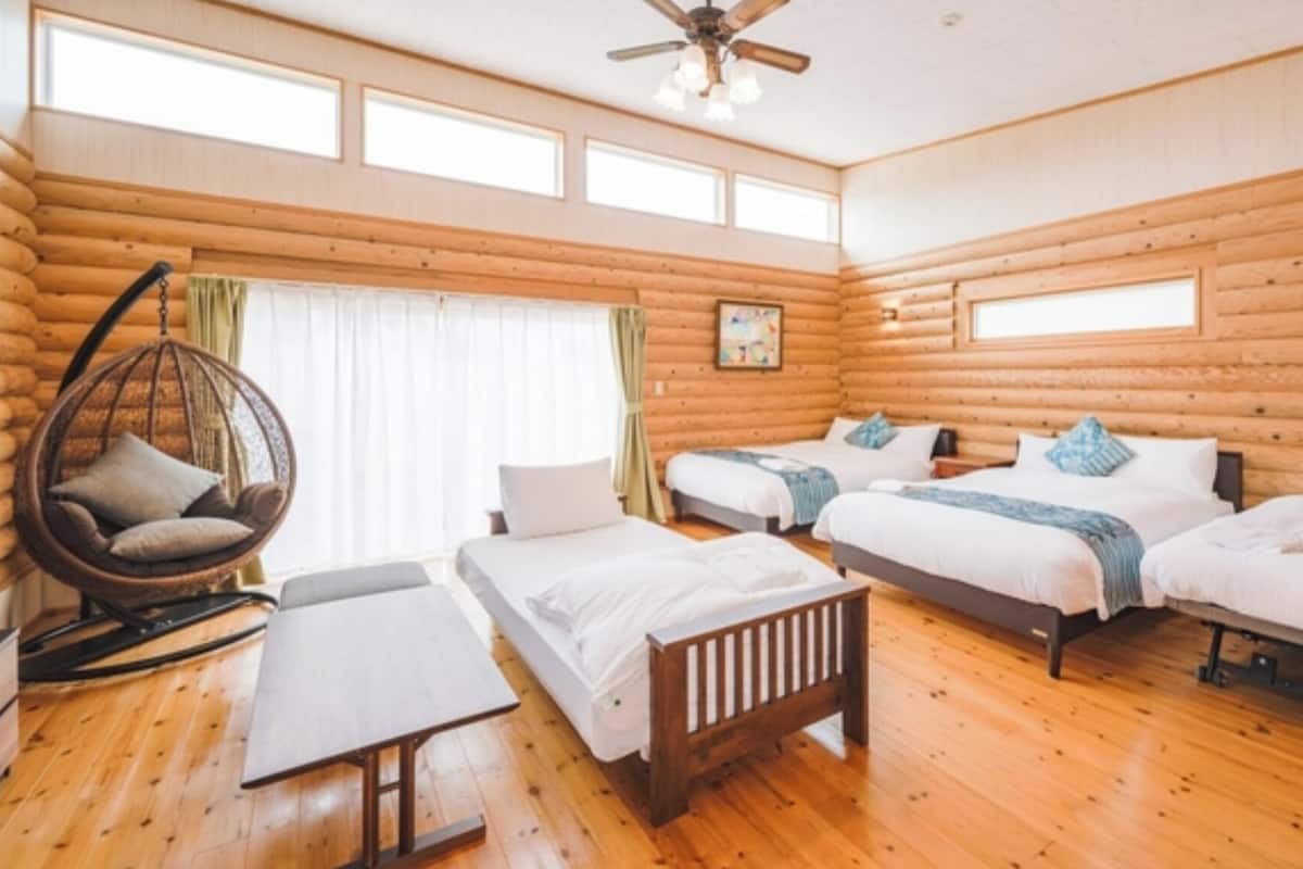 Una habitación de estilo cabaña con dos camas, un sillón colgante y suelo de madera.