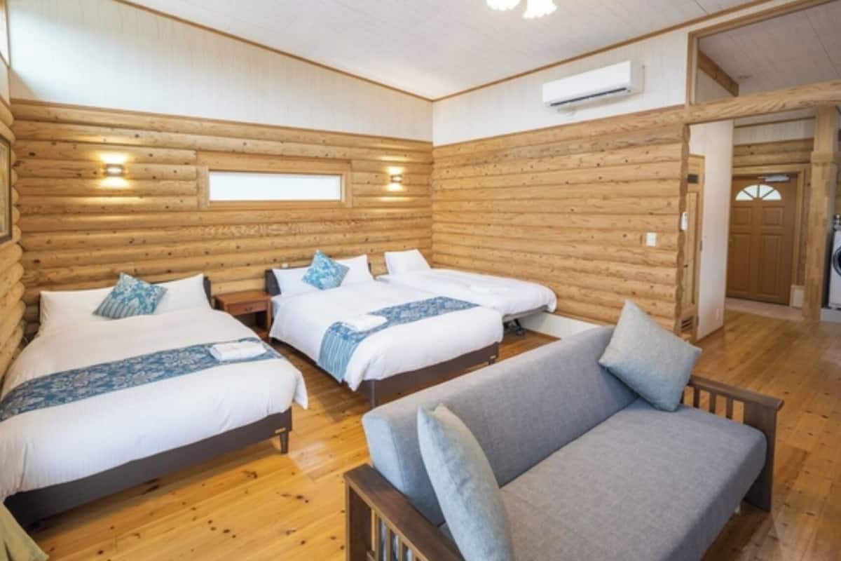 Una habitación tipo cabaña de madera con tres camas, un sofá y una lavadora.
