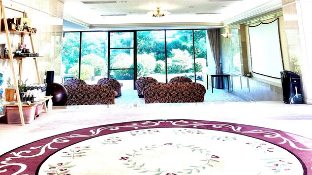 Eine großzügige Lobby mit hoher Decke, einem großen Kronleuchter und Blick auf Grün hinter den Fenstern.