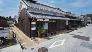Un bâtiment traditionnel japonais, doté d’un toit en tuiles, de murs en bois et d’un petit jardin agrémenté d’une plante en pot.