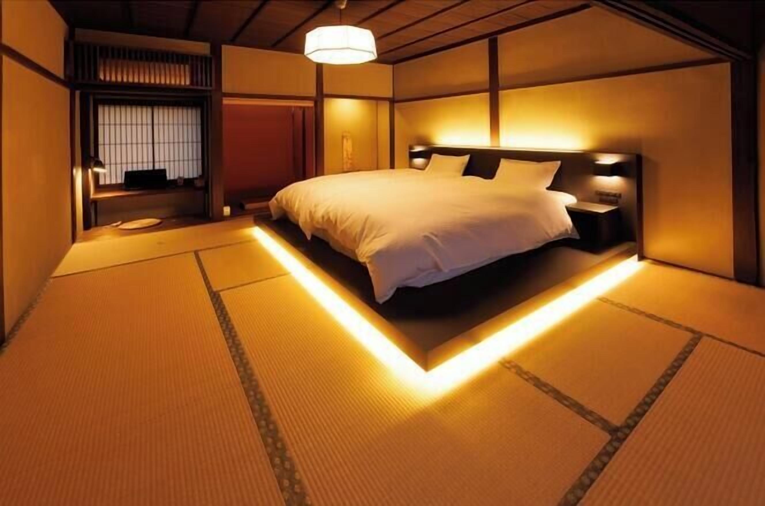 A traditional Japanese-style bedroom with tatami flooring, a low platform bed, and a sliding shoji screen door.