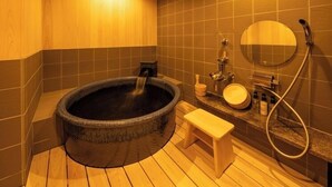 Un sauna équipé d’un bain à remous en pierre, d’un banc en bois et d’un miroir avec pomme de douche.