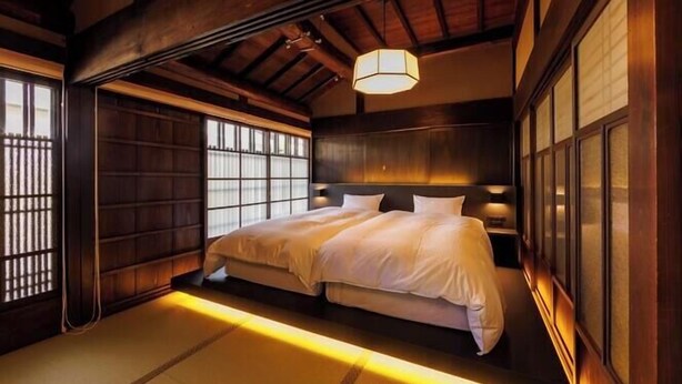 Une chambre de style japonais traditionnel, avec un sol recouvert de tatamis, un lit bas doté d’une tête de lit en bois et des portes coulissantes.