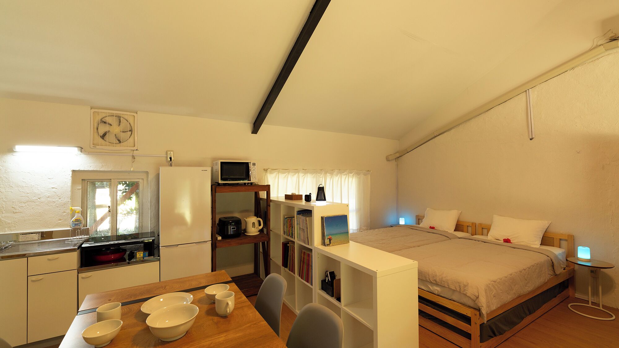A compact bedroom with a bed, bedside table, and a small desk area with a computer and books.