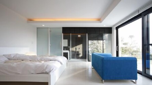 Ein modernes Schlafzimmer mit einem großen Bett, einem blauen Sessel und Blick durch eine Glastür.