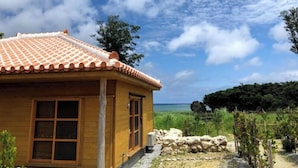 A wooden house with a tiled roof, a window, and a view of the sea. - Tabinoteitaku Okinawa Nakijin Homann Concept (Nakijin)