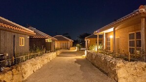 A pathway leading to a row of traditional wooden buildings with tiled roofs, surrounded by stone walls. - Tabinoteitaku Okinawa Nakijin Homann Concept (Nakijin)