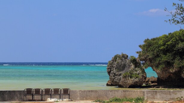 A coastal view with a seating area and a large rock formation. - Tabinoteitaku Okinawa Nakijin Homann Concept (Nakijin)
