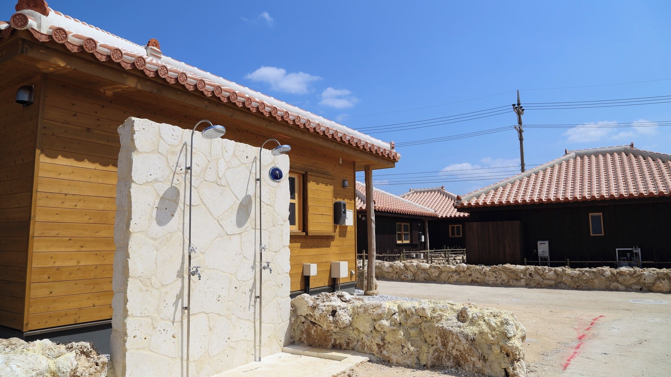 Edificio de madera con techo de tejas, pared de piedra y zona pavimentada con una línea roja.