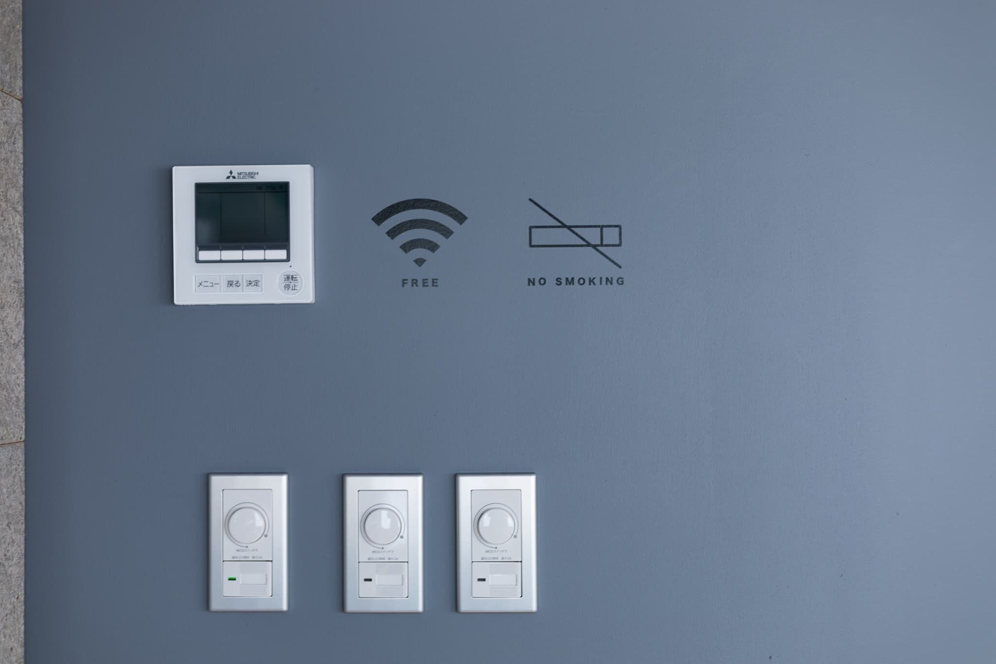 Een muur met een thermostaat, een Wi-Fi symbool, een rookverbodsge teken en nog eens drie thermostaten.
