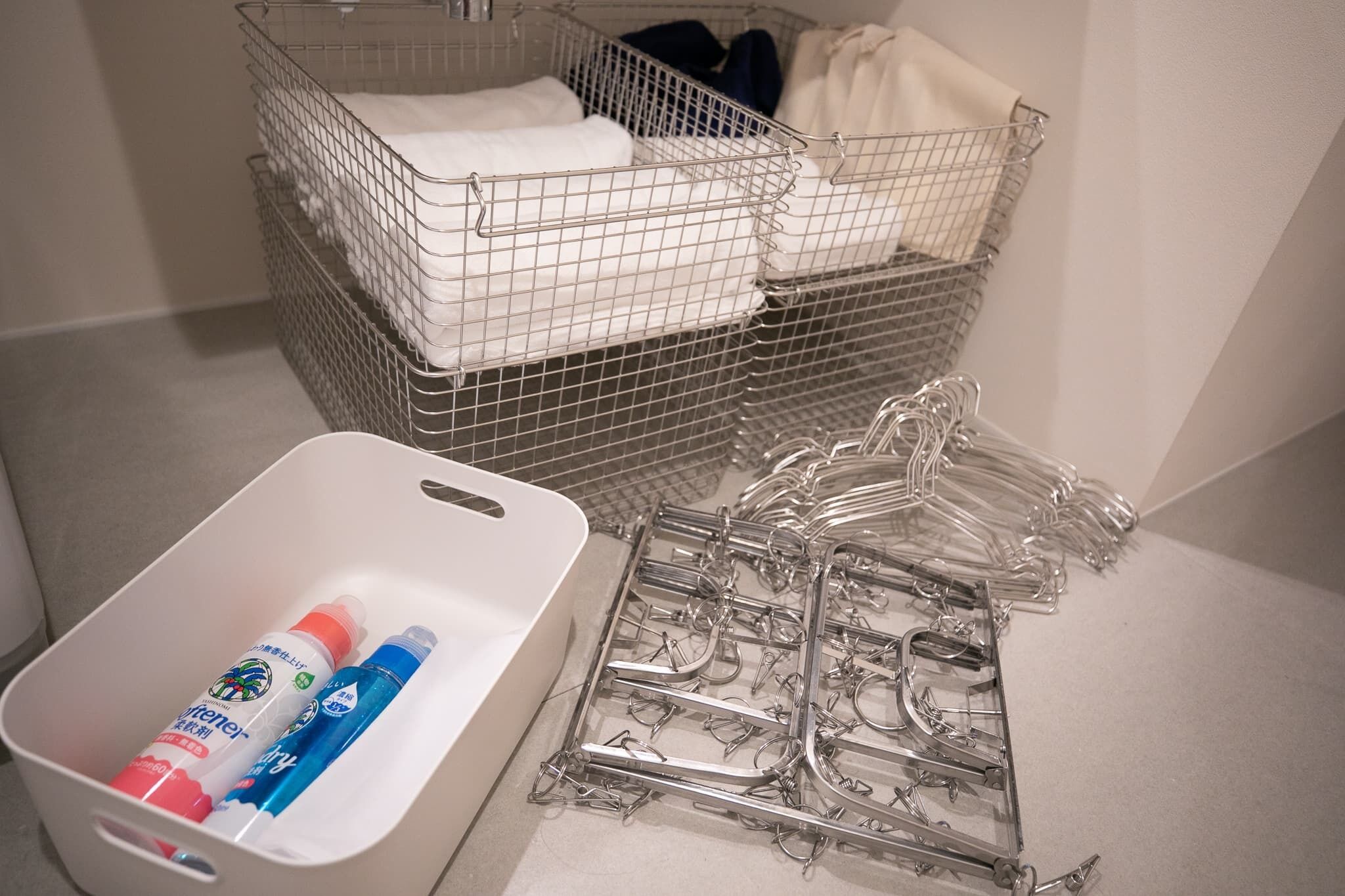 Un espace de rangement avec des paniers en fil métallique contenant des serviettes pliées et un récipient avec des produits de nettoyage.