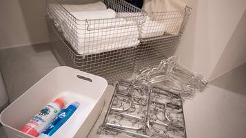 Un espace de rangement avec des paniers en fil métallique contenant des serviettes pliées et un récipient avec des produits de nettoyage.