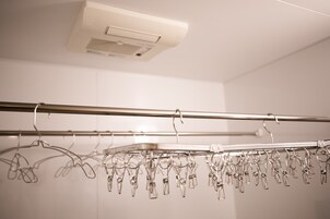 A metal clothing rack with multiple hangers and clips in a room with white walls and a ceiling vent.