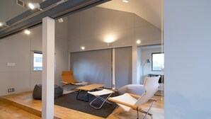 Un espace de bureau moderne avec un plancher en bois, des murs blancs et une grande fenêtre. On y trouve plusieurs chaises et tables disposées pour les réunions.