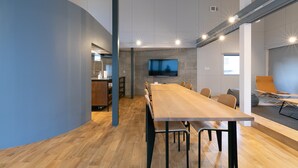 Une salle de conférence moderne, avec une longue table, des chaises, un téléviseur à écran plat et un coin cuisine à l’arrière-plan.