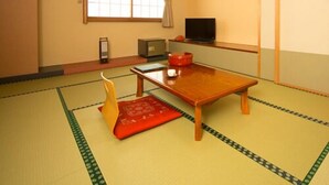 A traditional Japanese room with tatami flooring, a low wooden table, a television, and a sliding door. - Hotel Shugetsukan (Akita)