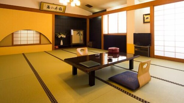 A tatami mat room with a low table, chairs, and a traditional Japanese-style ceiling light. - Hotel Shugetsukan (Akita)