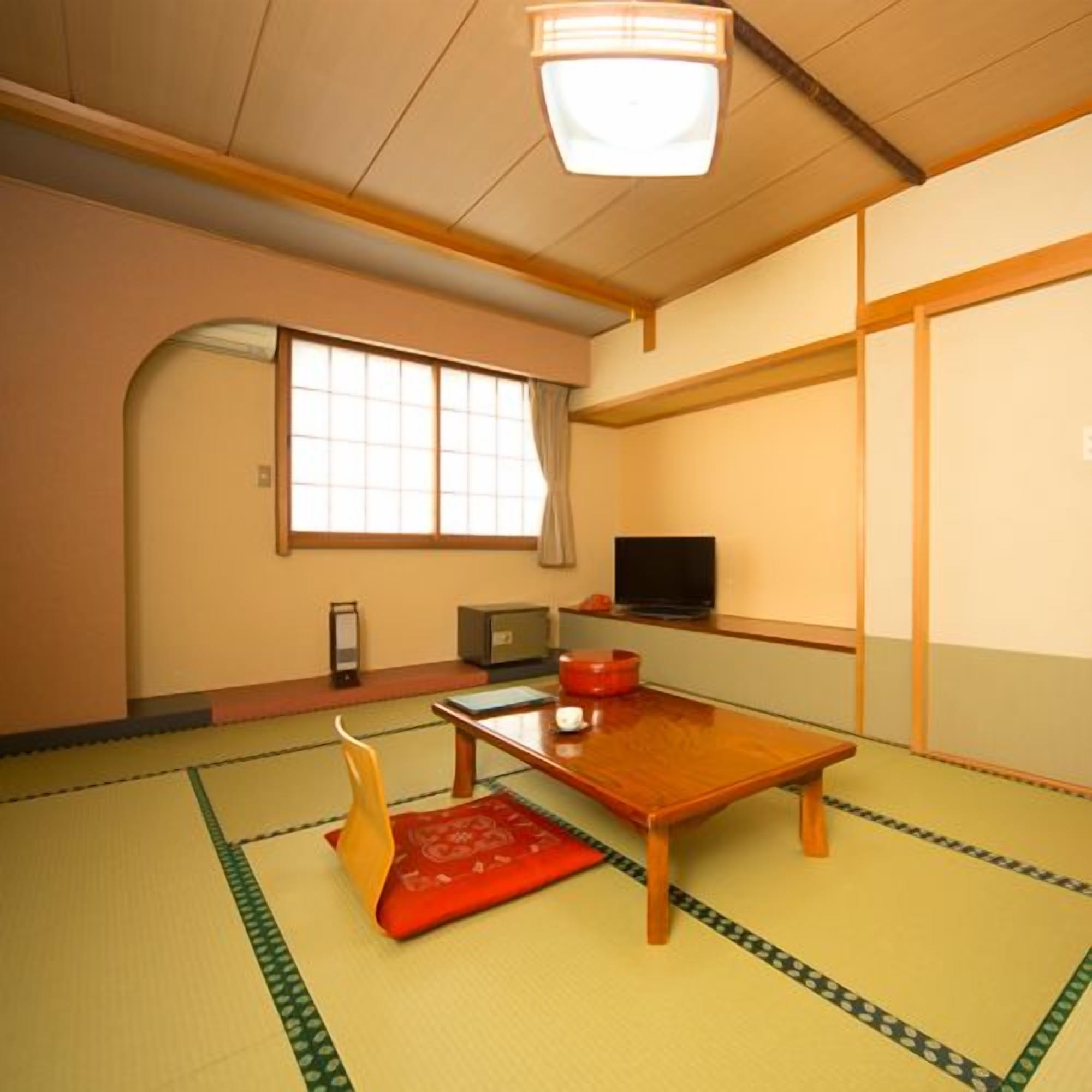 A traditional Japanese room with tatami flooring, a low wooden table, a television, and a sliding door.