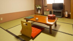 A traditional Japanese room with tatami flooring, a low table, a cushioned bench, a television, and a sliding door leading to another room. - Hotel Shugetsukan (Akita)