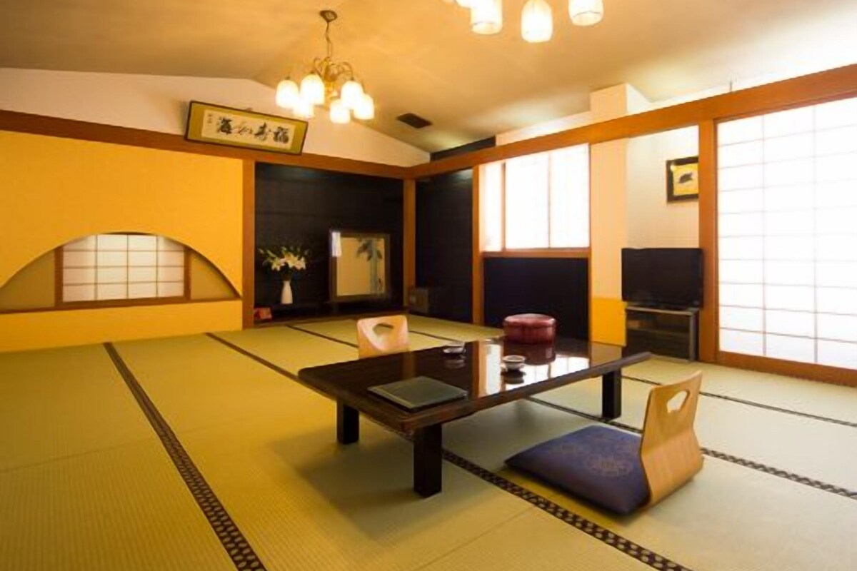 A tatami mat room with a low table, chairs, and a traditional Japanese-style ceiling light.