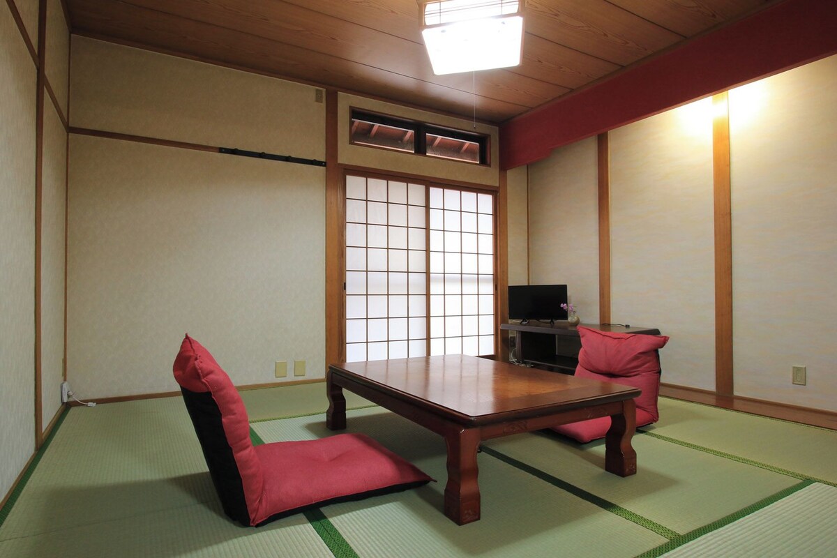 A traditional Japanese room with tatami flooring, a low wooden table, and red cushions.